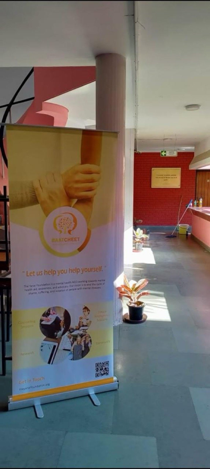 A Baatcheet banner set up in a campus corridor, carrying the line "Let us help you help yourself" and a QR code.