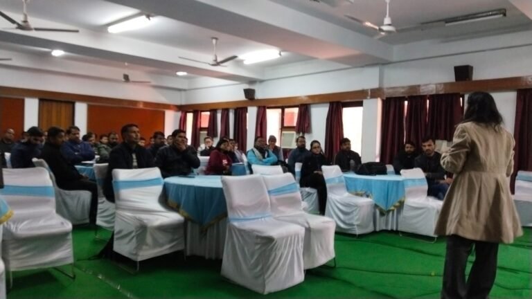 A full hall of seated attendees listens to a speaker standing at the front of the room.